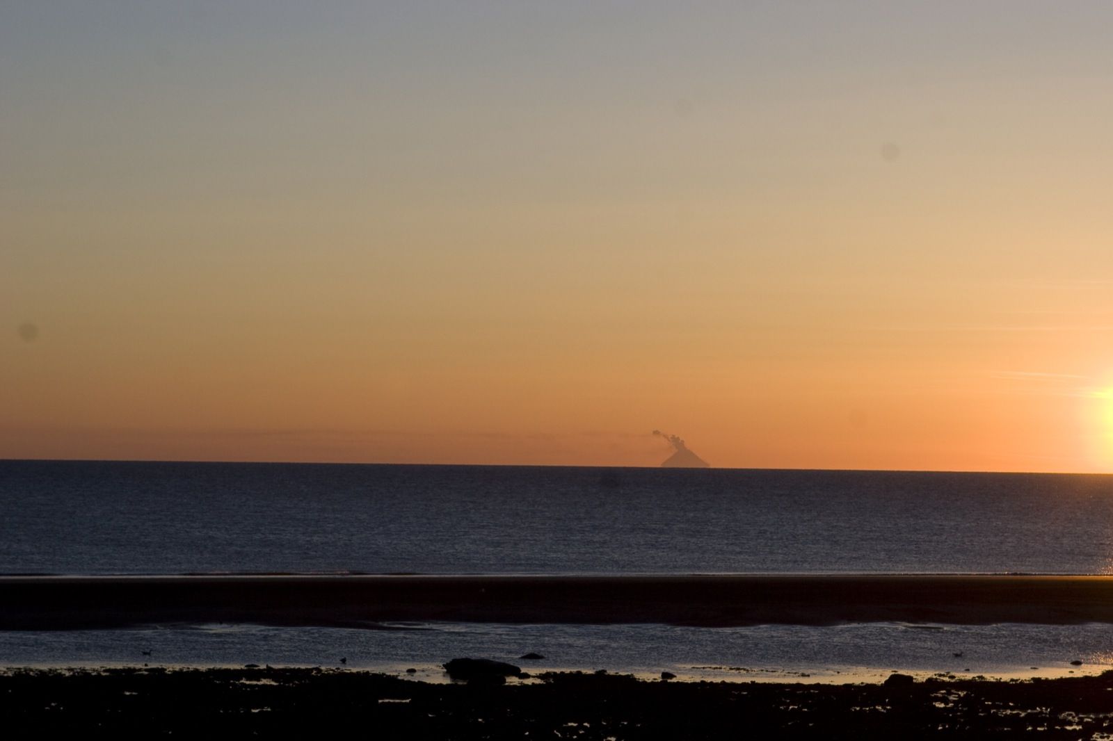 The sun setting over Cook Inlet seen from the Homer Spit, with the faint cone of Augustine Volcano on the horizon