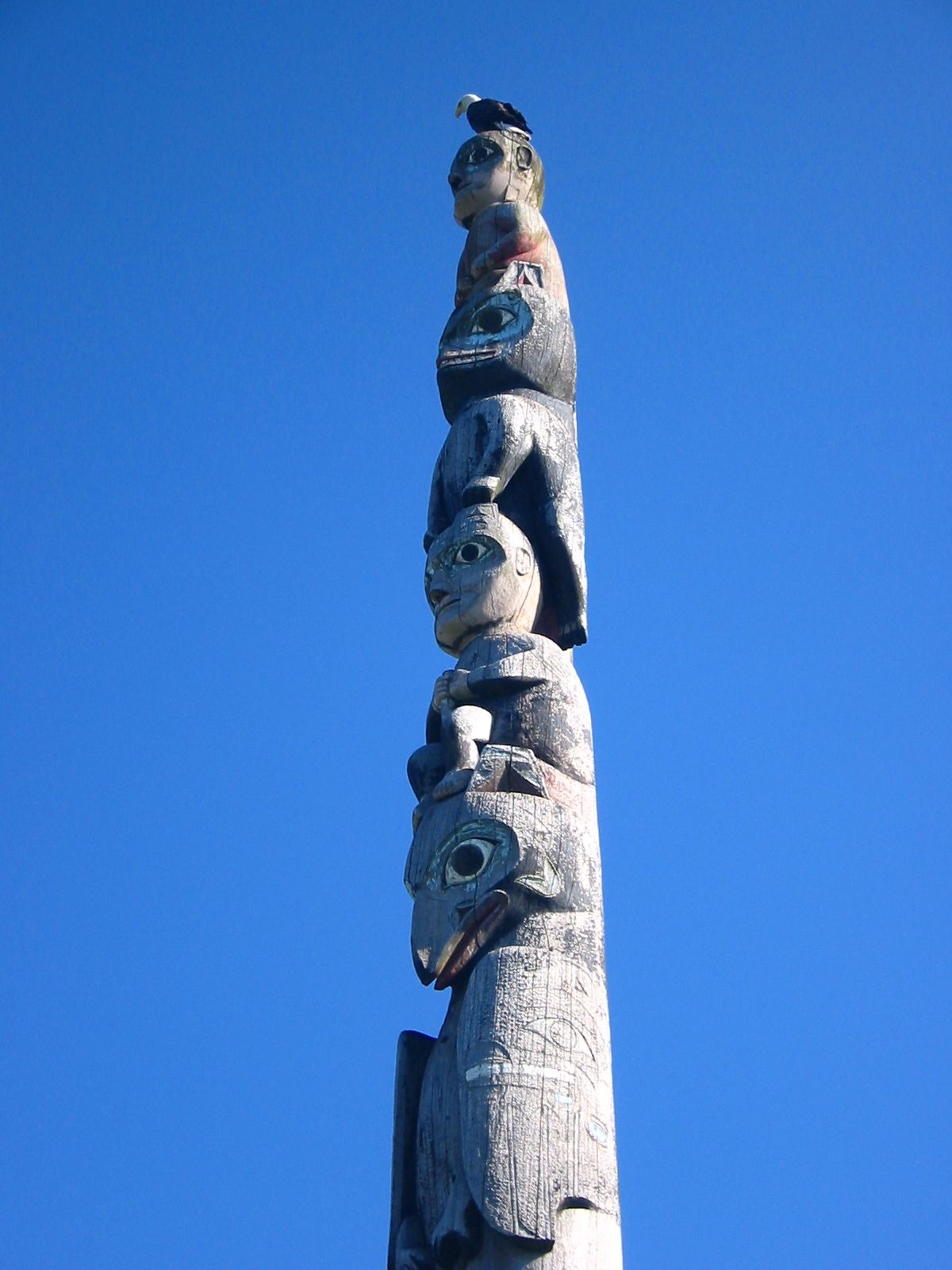A bald eagle perched on top of a carved totem pole in Sitka against a blue sky
