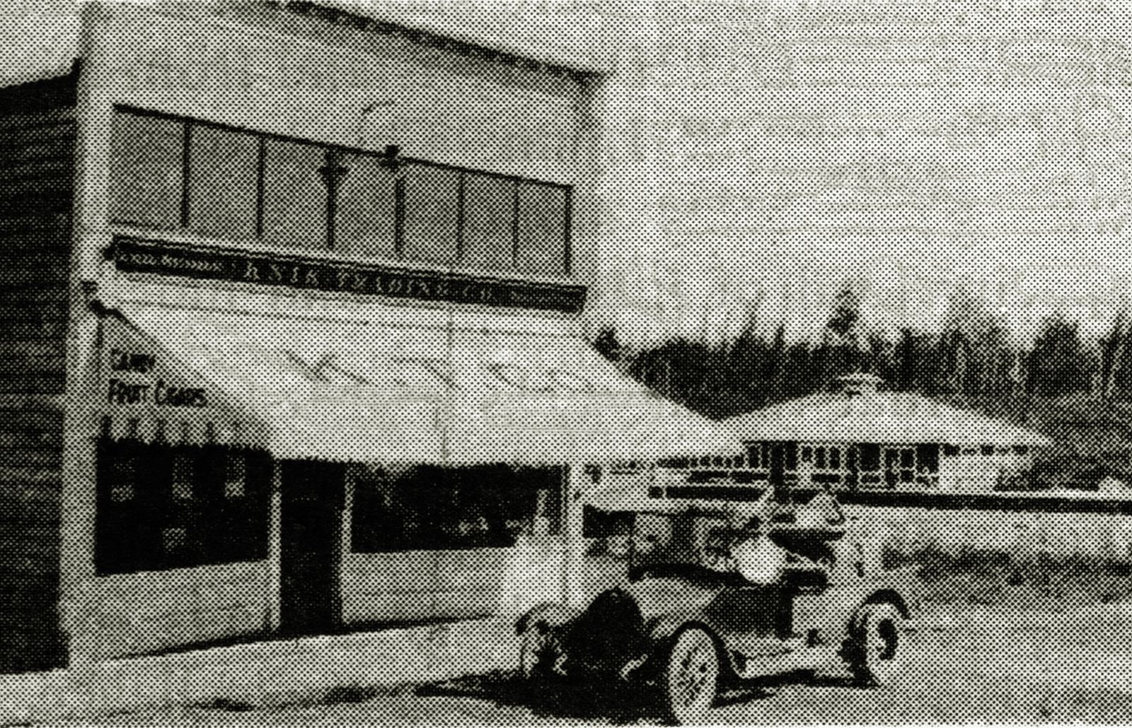 Black and white photo of a storefront and an early automobile at the foot of Main Street in Wasilla in the early 1920s