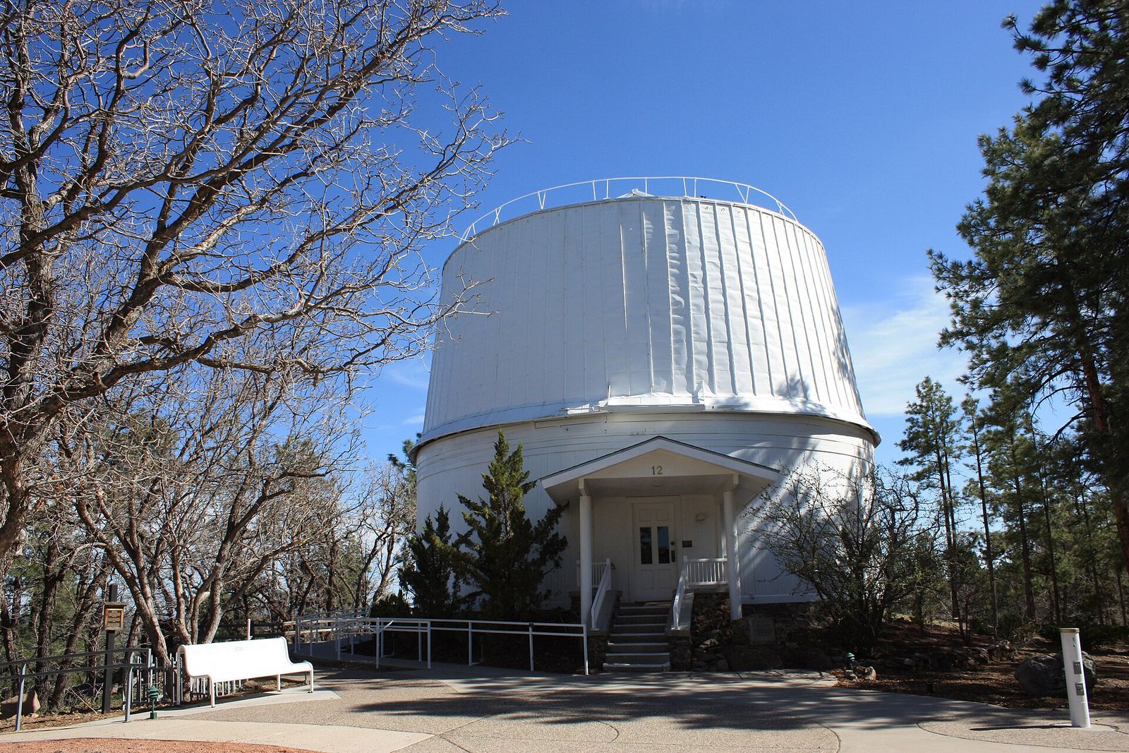 The white Alvan Clark telescope dome at Lowell Observatory in Flagstaff, framed by ponderosa pines and bare oak branches