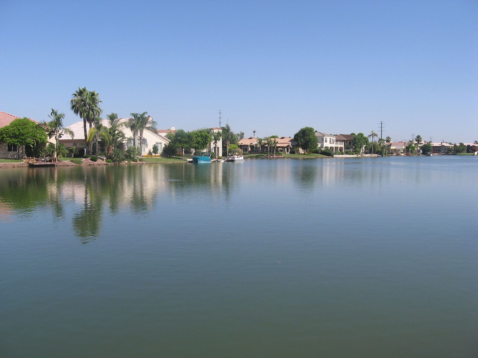 Homes and palm trees reflected in the lake at Val Vista Lakes in Gilbert under a clear sky