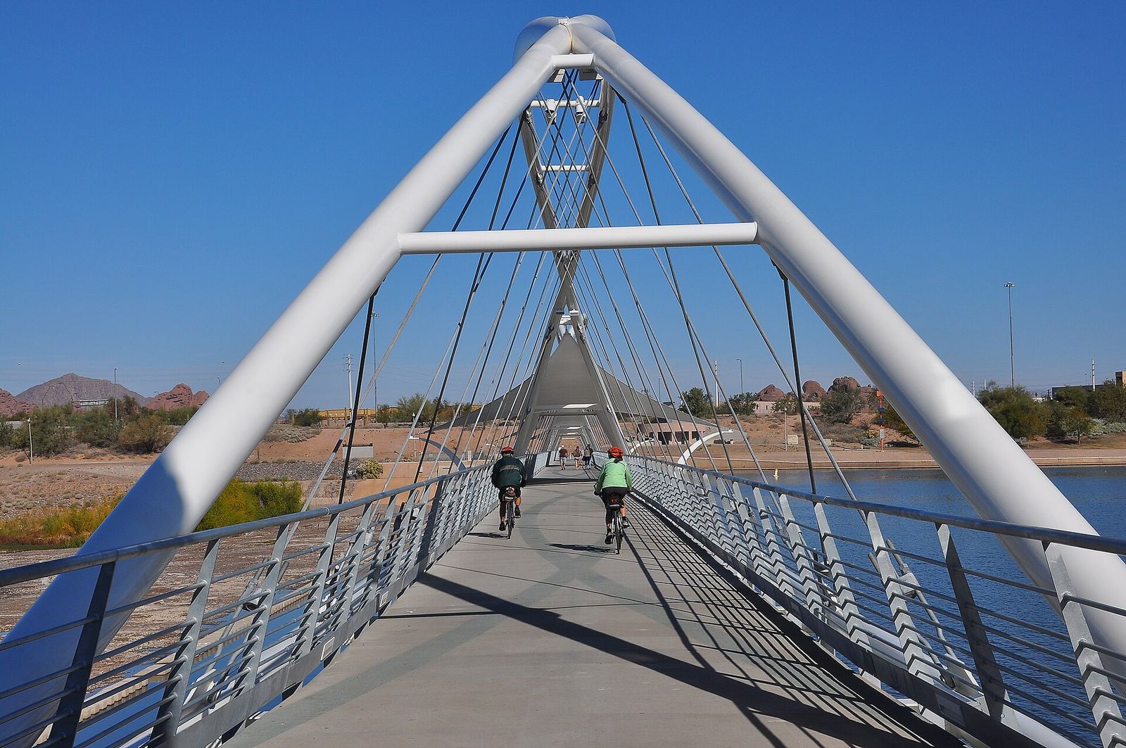 Cyclists crossing the white arched pedestrian and bike bridge at the Tempe Town Lake dam
