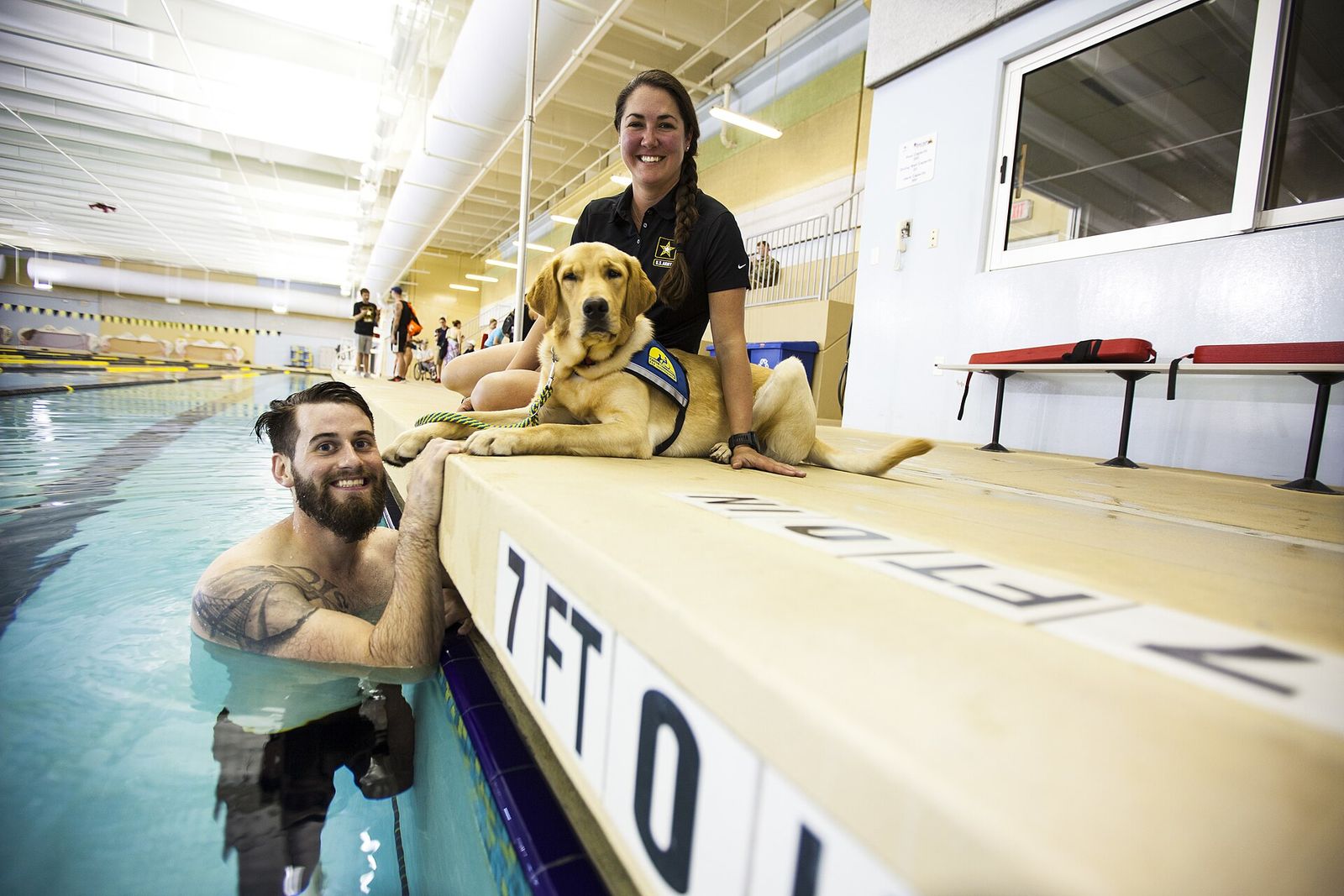 A U.S. Army veteran in a pool beside a service dog lying on the deck during the 2016 Army Trials at Fort Bliss