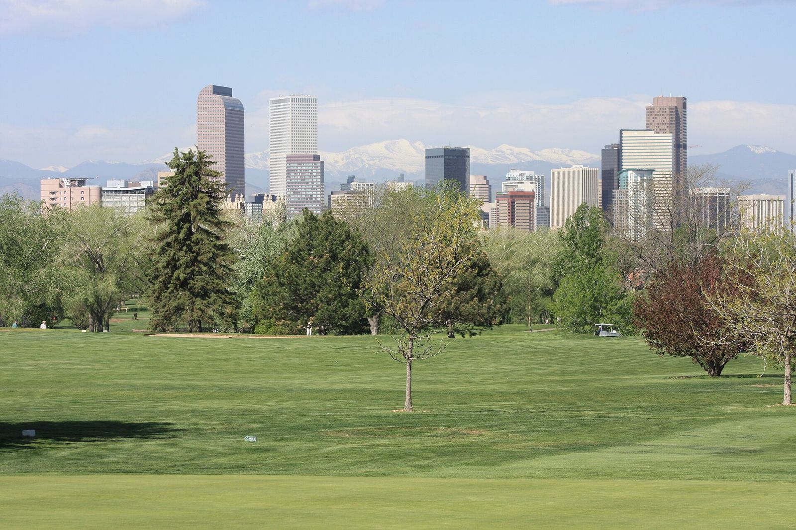 Downtown Denver's towers behind the trees and lawns of City Park Golf Course, with Mount Evans on the horizon