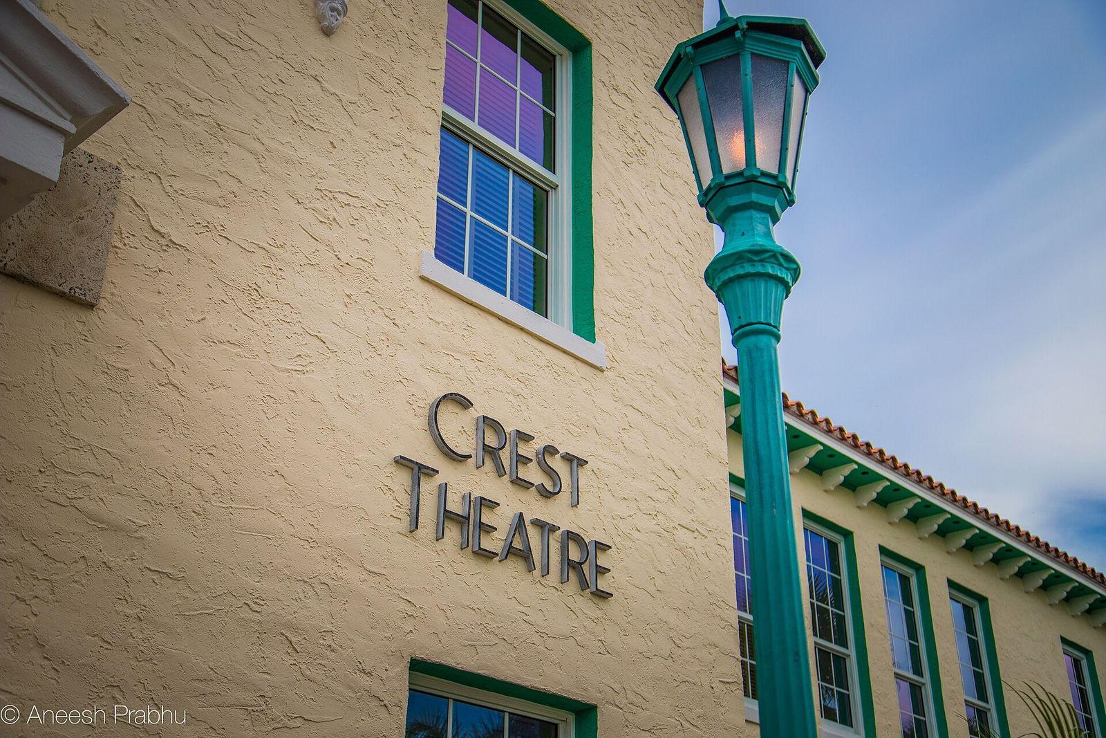 The cream stucco wall of the Crest Theatre in Delray Beach, with its name in raised letters, green-trimmed windows and a teal lamppost
