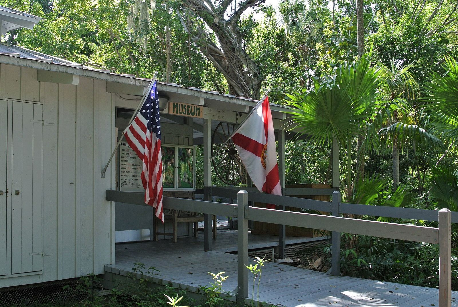 The small white Arch Creek museum building with American and Florida flags on its porch among tropical trees in North Miami