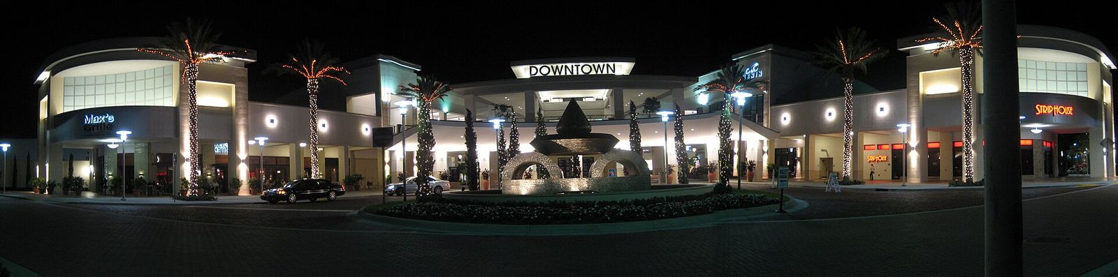 A wide night view of the lit main entrance and storefronts of Downtown at the Gardens in Palm Beach Gardens