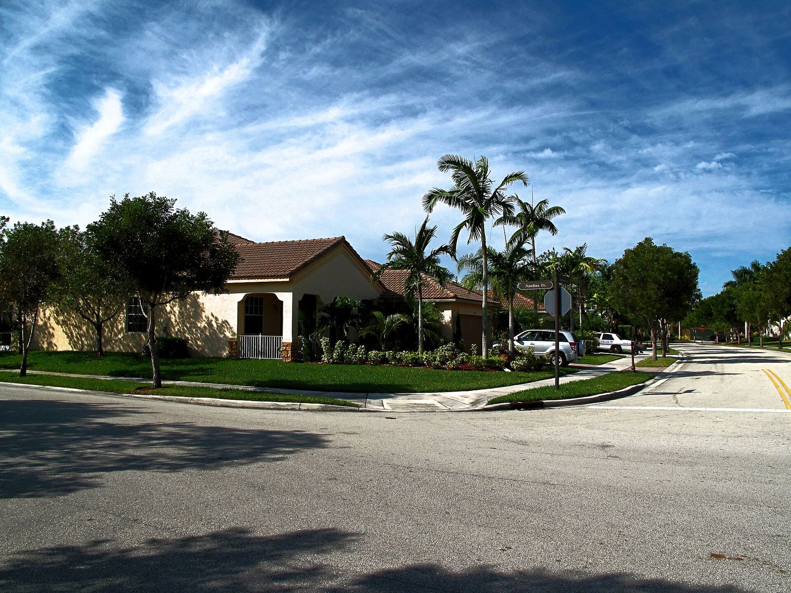A quiet Weston residential street on Nandina Drive with a tile-roofed house, palms and a deep blue sky