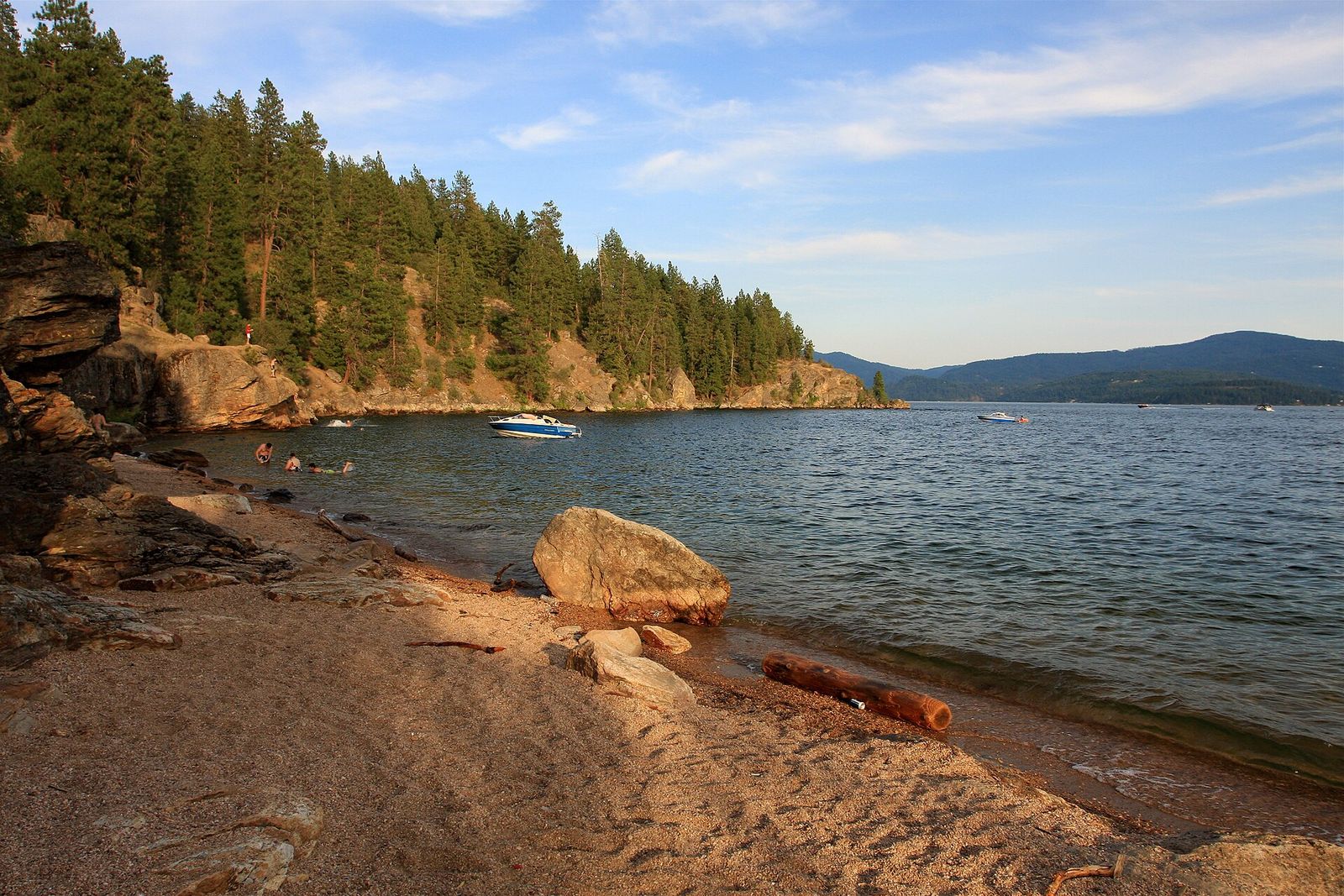 A small sandy beach and boulders below the forested slope of Tubbs Hill on Lake Coeur d'Alene