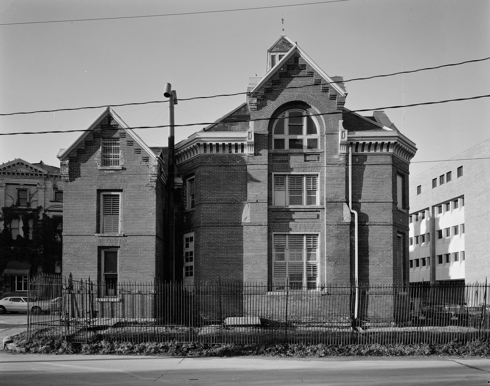 The brick Pottawattamie County Squirrel Cage Jail in Council Bluffs behind an iron fence, in a black-and-white photograph