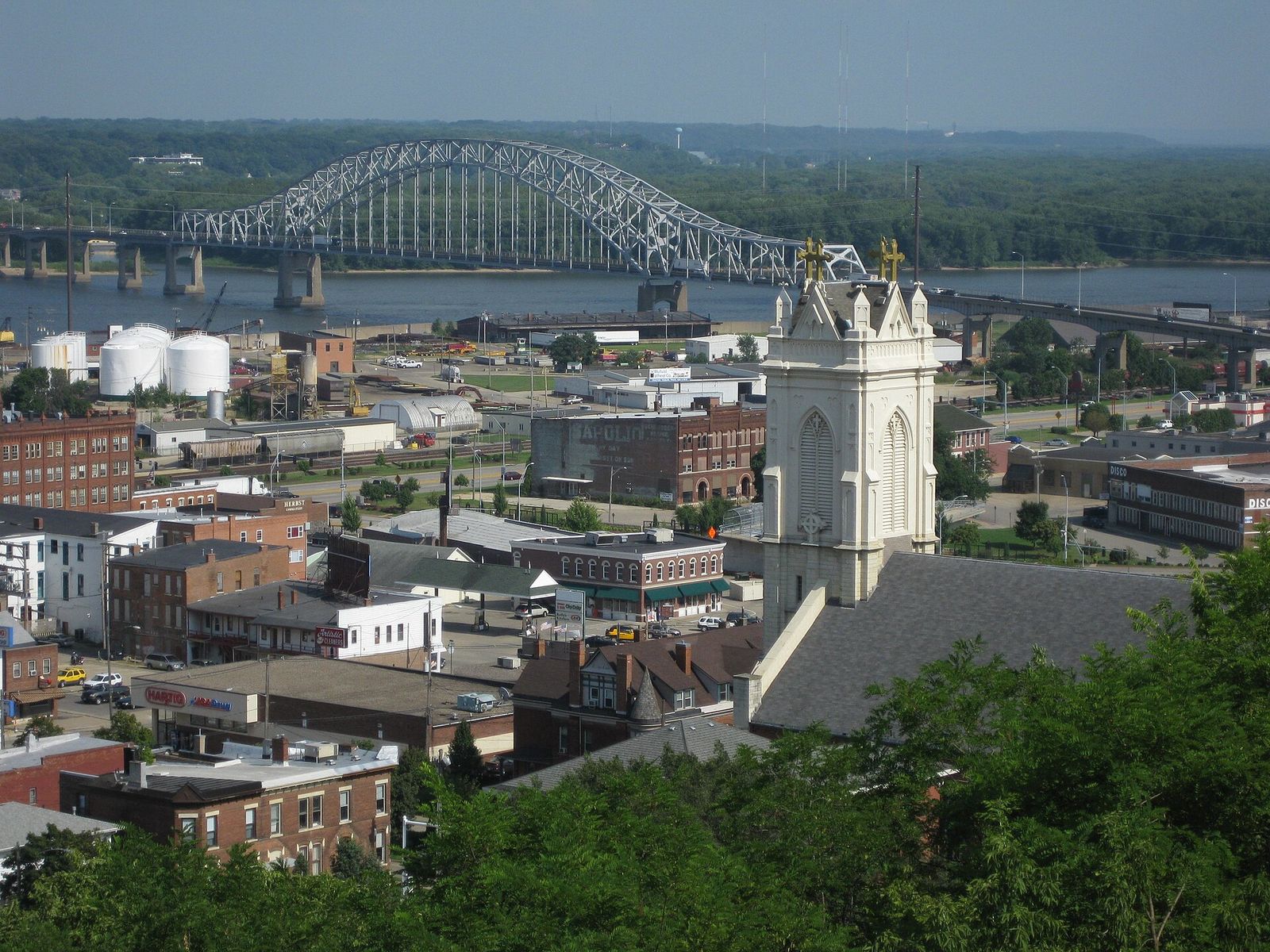 Downtown Dubuque seen from a bluff, with church spires, brick buildings and the arched Julien Dubuque Bridge over the Mississippi River