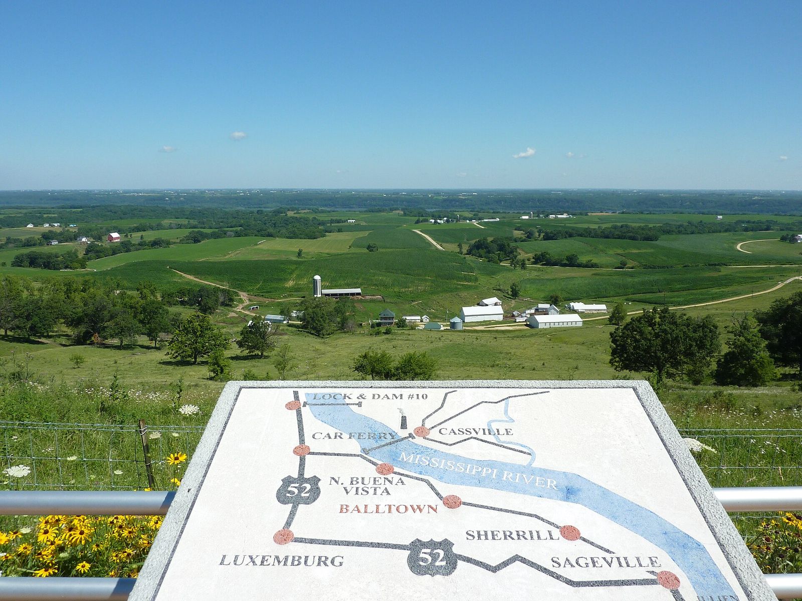 Green farm fields and the Mississippi River valley seen from the scenic overlook in Balltown, Iowa, with a painted map in front