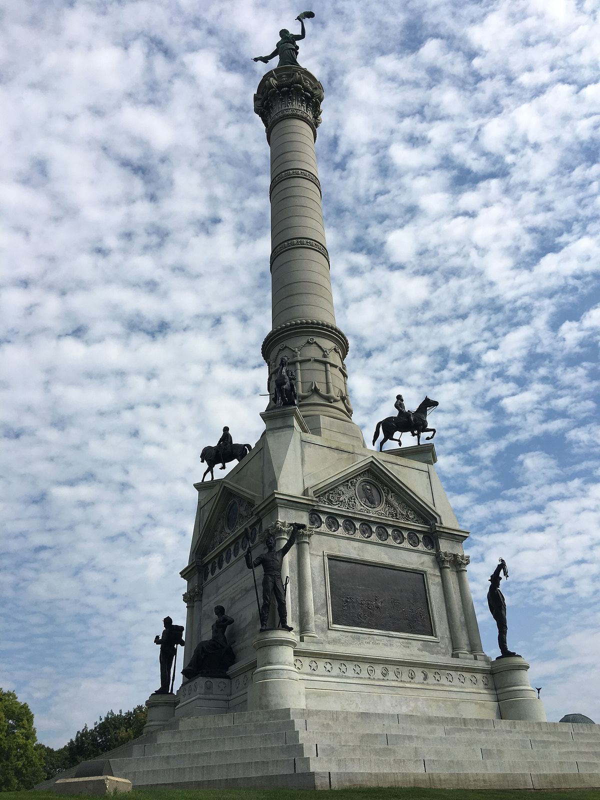 The Iowa Soldiers' and Sailors' Monument in Des Moines, a tall granite column with bronze figures, against a cloud-streaked sky