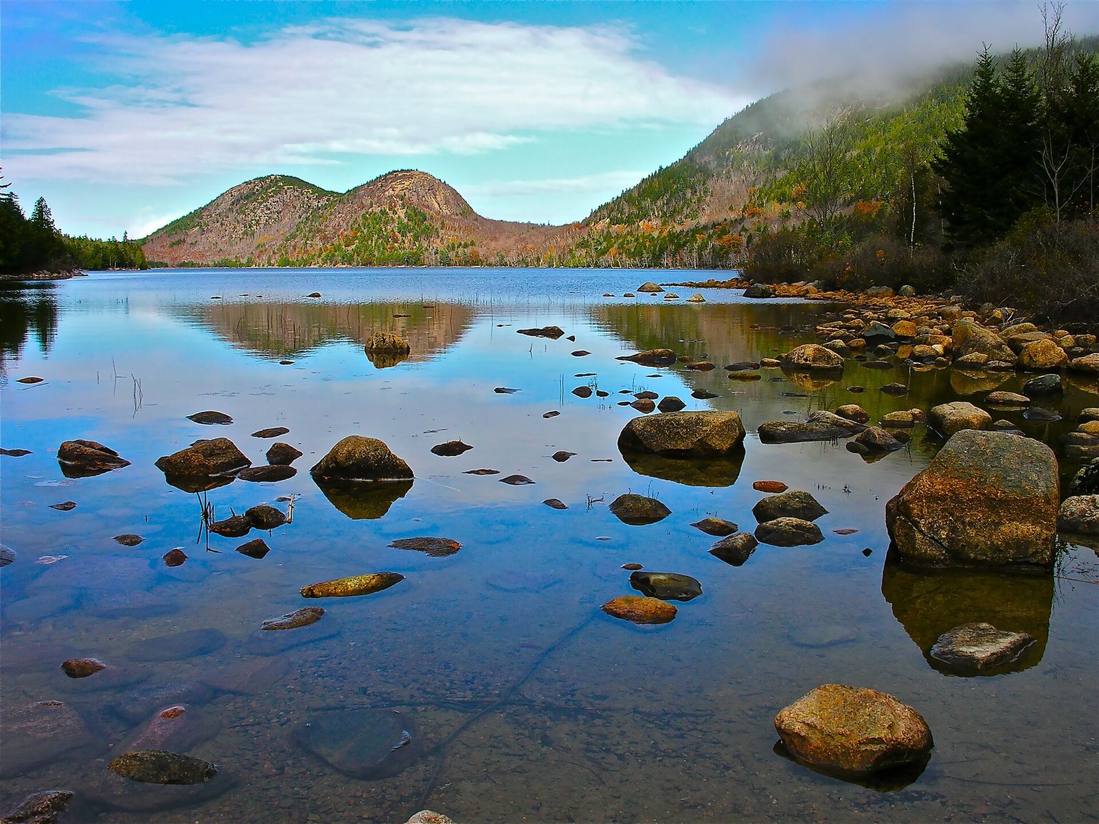 Jordan Pond in Acadia National Park, with smooth rocks in the clear water and the rounded Bubbles hills behind