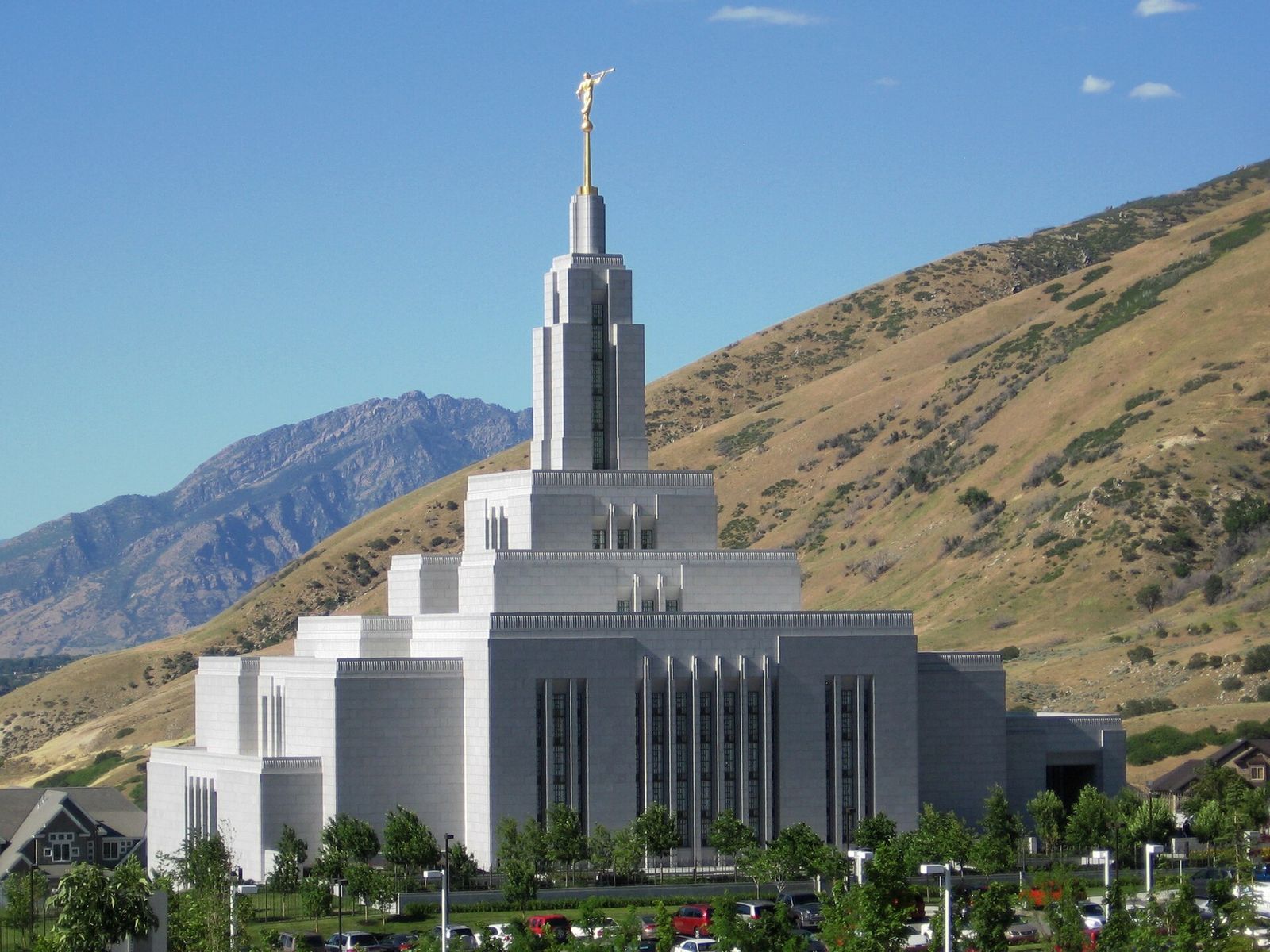 The white Draper Utah Temple and its spire against dry foothills and a blue sky