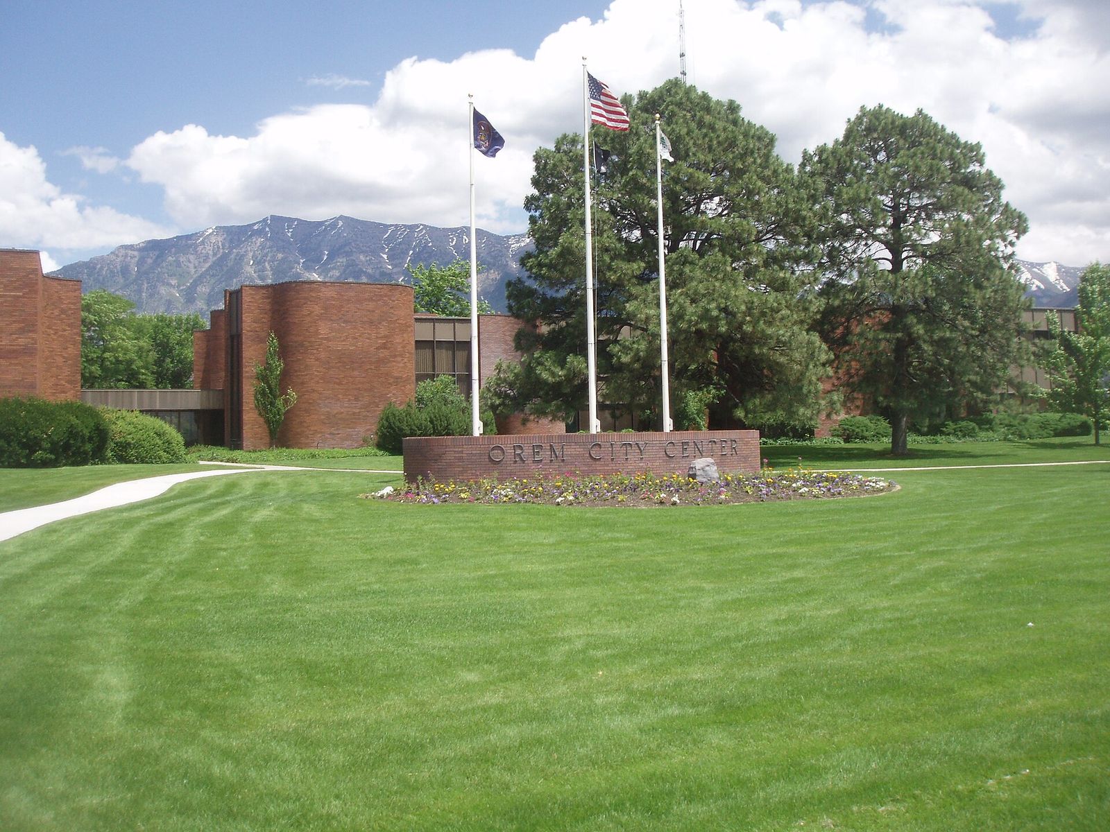 Orem City Center, a low brick building behind a green lawn and flagpoles, with mountains beyond