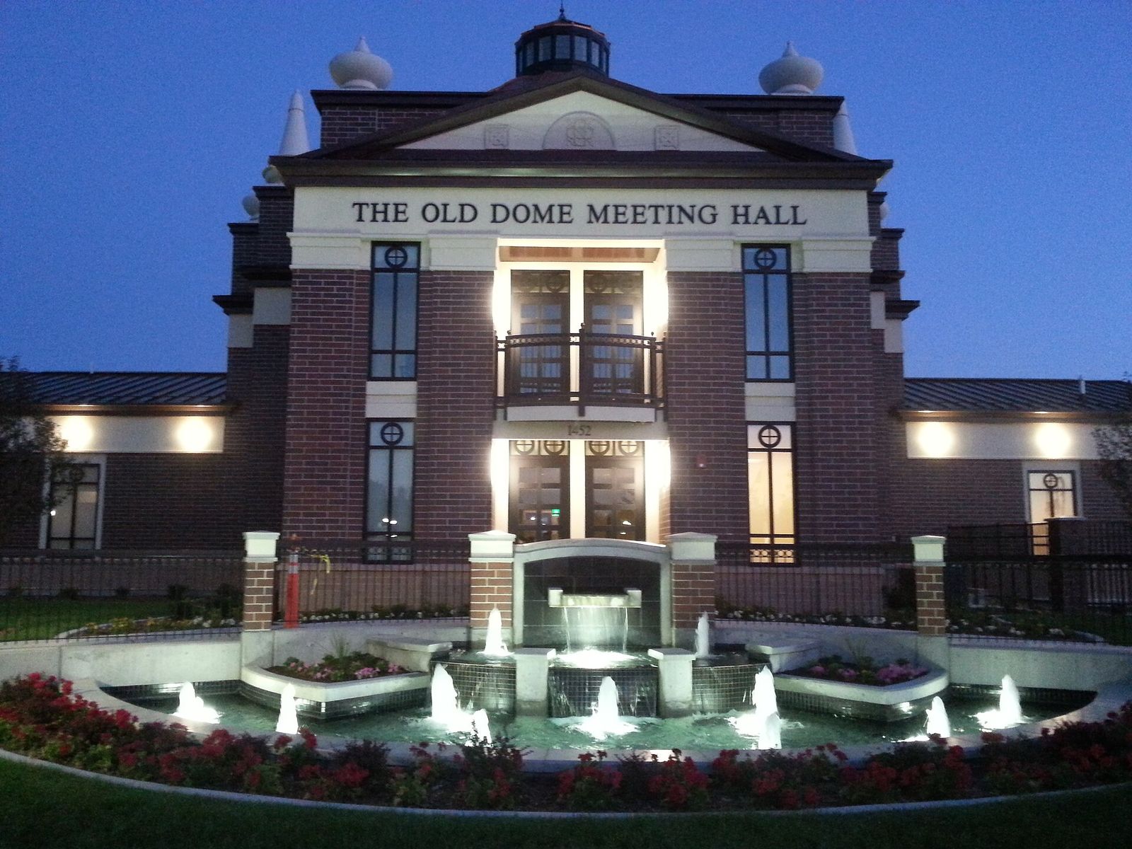 The Old Dome Meeting Hall in Riverton City Park, lit at dusk behind a fountain