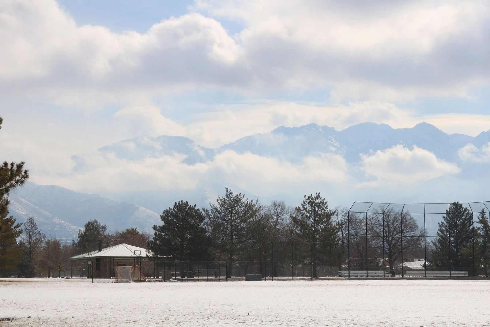 Snow on the lawns of Sugar House Park, with pines and the Wasatch Range behind