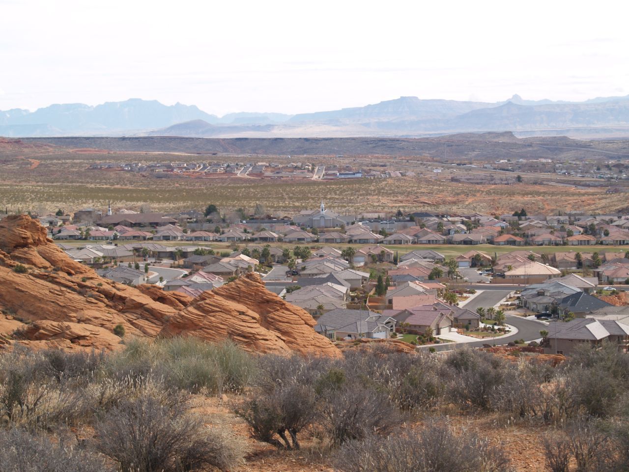 Rooftops of Washington spread across the valley below red sandstone, with mountains on the horizon